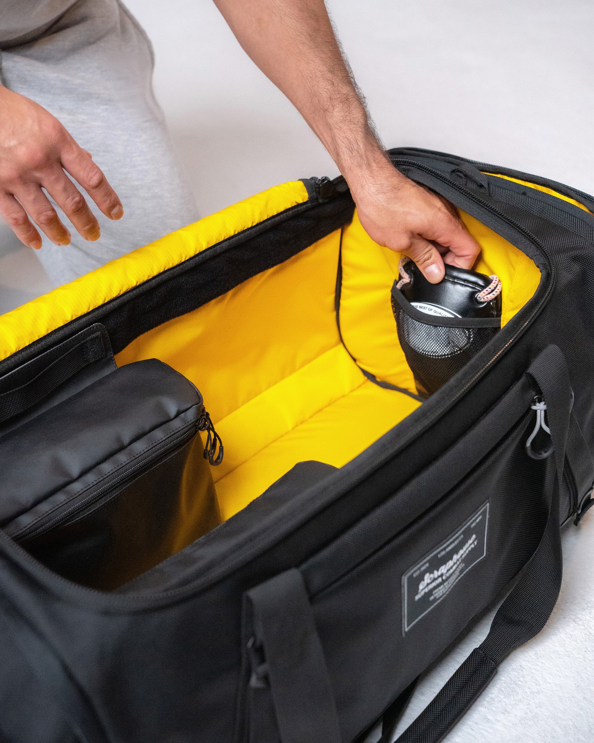 Hand tucking a glove into the interior mesh pocket beside the duffle's yellow ripstop lining