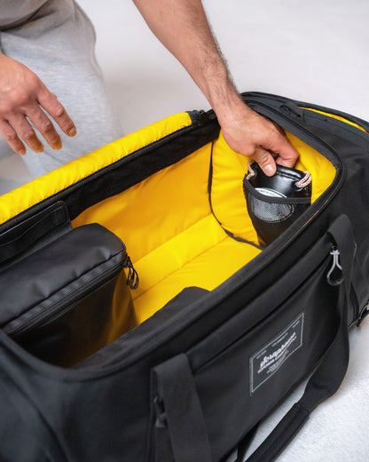 Hand tucking a glove into the interior mesh pocket beside the duffle's yellow ripstop lining