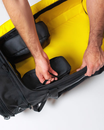 Hands arranging zippered saddleboxes inside the duffle's hi-vis yellow main compartment